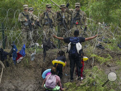 A migrant gestures to Texas National Guards standing behind razor wire on the bank of the Rio Grande river, seen from Matamoros, Mexico, Thursday, May 11, 2023. Pandemic-related U.S. asylum restrictions, known as Title 42, are to expire May 11. (AP Photo/Fernando Llano)