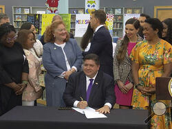 In this screenshot from a livestream broadcast by the State of Illinois, Gov. J.B. Pritzker signs a bill, Monday, June 12, 2023, at Harold Washington Library's Thomas Hughes Children's Library in downtown Chicago. The new law will require the state's libraries to uphold a pledge not to ban material because of partisan disapproval, starting on Jan. 1, 2024. If they refuse, they will not receive state funding. Pritzker said the law will make Illinois the first state in the nation to outlaw book bans. (State o