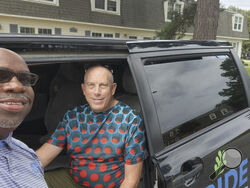 Driver Milton Barnes poses for a photo with customer David Bunn in front of his RIDE van in Wilson, N.C. on Aug. 24, 2023. The city of Wilson, North Carolina, ended its bus service in September 2020 to offer on-demand van trips anywhere in town for less than $3 a ride. Even during the pandemic, which sent public transit ridership plummeting, it surged 300% in Wilson. (Courtesy of Milton Barnes via AP)