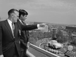 FILE - In this May 18, 1964, file photo Gov. George Romney and his son, Mitt, look out over the New York World's Fair grounds from the heliport after attending a Michigan breakfast at the Top of the Fair Restaurant. The governor and a large delegation from Michigan were there for Michigan Day at the fair. At right is part of the Chrysler exhibit and behind them is the Ford exhibit. (AP Photo, File)