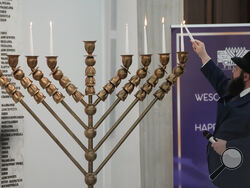 A rabbi lights candles of a menorah again after an incident in which a far-right lawmaker put out the candles, in Warsaw, Poland, on Tuesday, Dec. 12, 2023. The speaker of the parliament, Szymon Holownia, denounced the incident that was carried out by Grzegorz Braun on Tuesday, and said there would be no tolerance for antisemitic and xenophobic behavior in the Sejm, the Polish parliament. (AP Photo/Czarek Sokolowski)