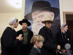 FILE - Anna Stoltzfus, left, talks with her husband Matthew Stolzfus in front of a portrait of the late Lubavitcher Rabbi Menachem Schneerson, while taking a tour with John Lapp, center, his son Jonathon, 6, and wife Priscilla, at a museum Tuesday, March 31, 2009 in the Crown Heights neighborhood of Brooklyn, New York. The city's ultra-Orthodox Jews took a group of Pennsylvania Amish on a walking tour of their world Tuesday, saying their communities are naturally drawn to each other with a commitment to sim