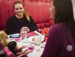 Marisa Dragos, 23, left, along with her childhood friend Lisa Costantino, 24, right, sit for lunch at American Girl Cafe with two store-borrowed dolls, Friday, Dec. 2, 2022, in New York. "I still have the dolls, just kind of sitting in my room," said Dragos about her American Dolls at home. "They are my little friends that I hang out with." (AP Photo/Bebeto Matthews)