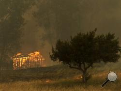 Fire engulfs a structure during a wildfire Thursday, May 15, 2014, in Escondido, Calif. One of the nine fires burning in San Diego County suddenly flared Thursday afternoon and burned close to homes, trigging thousands of new evacuation orders. (AP Photo/Gregory Bull)