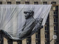 Men hang a giant banner with a picture of Cuba's late leader Fidel Castro as a young revolutionary, from the Cuban National Library building in Havana, Cuba, Sunday, Nov. 27, 2016. Cuba's government declared nine days of national mourning after Castro died Friday and this normally vibrant city has been notably subdued. (AP Photo/Desmond Boylan)