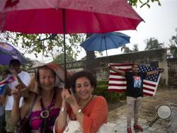 A handful of Cubans gather along the Malecon sea wall under a steady rain to wave to U.S. President Barack Obama's convoy before it arrives in Old Havana, Cuba, Sunday, March 20, 2016. Obama's trip is a crowning moment in his and Cuban President Raul Castro's ambitious effort to restore normal relations between their countries. (AP Photo/Rebecca Blackwell)