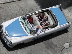 In this May 13, 2015 photo, tourists ride a classic American convertible in Havana, Cuba. The thaw in relations between the U.S. and Cuba has led to a dramatic 36 percent increase in visits by Americans to Cuba since January compared to the same period last year, along with a 14 percent rise in arrivals from around the world. (AP Photo/Desmond Boylan)