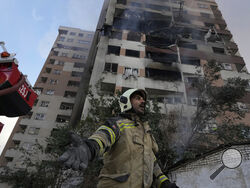 A firefighter calls out his colleagues at the scene of an explosion in a residence compound in northern Tehran, Iran, Friday, June 13, 2025. (AP Photo/Vahid Salemi)