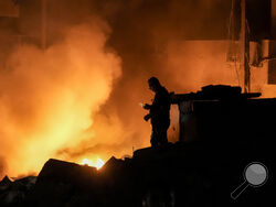 A man uses his mobile phone as flames and smoke rise at the scene of buildings hit by an Israeli airstrike in central Beirut, Lebanon, Thursday, Oct. 10, 2024. (AP Photo/Bilal Hussein)