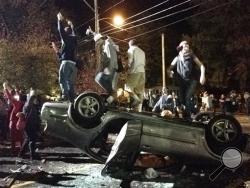 People stand atop an overturned car in Keene, N.H. on Saturday, Oct. 18, 2014, during a night of violent parties that led to destruction, dozens of arrests and multiple injuries, near the city's annual pumpkin festival. The parties around the school coincided with the annual Keene Pumpkin Festival, where the community tries to set a world record of the largest number of carved and lighted jack-o-lanterns in one place. (AP Photo/The Boston Globe, Jeremy Fox)