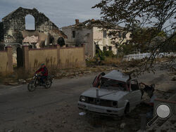 A man drives his motorcycle past a destroyed car in the retaken village of Velyka Oleksandrivka, Ukraine, Wednesday, Oct. 12, 2022. (AP Photo/Leo Correa)