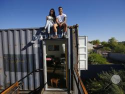 In this Wednesday, March 16, 2016, photo, Patrick Tupas, right, with his wife, Maria Real-Tupas, sit on the roof of their shipping container apartment, as their dog Moon Moon Fitzgerald stands at the front door, in Phoenix. In the Containers on Grand project, the apartments are designed in a way that retains the corrugated metal exteriors. Each unit is made of two containers, but inside there are no signs of the cargo hauling days. (AP Photo/Ross D. Franklin)