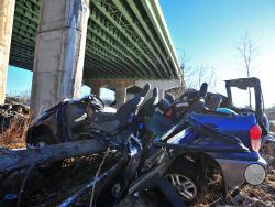 A SUV that catipulted off an Interstate 80 bridge overhead lies in a heap along the banks of the Hackensack River, Friday, Feb. 13, 2015, in Hackensack, N.J. The driver, swerving to avoid striking another vehicle on a highway, hit a snowbank along a guardrail and catapulted 60 feet off a bridge. Incredibly, authorities say, the two occupants suffered only minor injuries, and the vehicle landed upright. (AP Photo/The Record of Bergen County, Marko Georgiev)