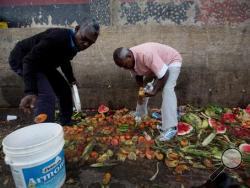In this May 31, 2016 photo, Pedro Hernandez, left, and his friend Luis Daza, pick up tomatoes from the trash area of the Coche public market in Caracas, Venezuela. At Coche, even once middle class Venezuelans made desperate by the country's economic collapse have taken to sifting through the trash to resell or feed themselves on discarded fruits and vegetables. (AP Photo/Fernando Llano)