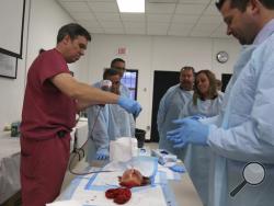 Dr. James Vosswinkel, left, the chief of trauma, emergency surgery, and surgical critical care, at Stony Brook University Hospital, demonstrates how to pack a gunshot wound on a fake body part during a first aid training session at Stony Brook University in New York, Tuesday, Nov. 29, 2016. A new federal initiative seeks to prevent deaths in terror attacks and school shootings by training ordinary people from custodians to administrators on how to treat gunshots, gashes and other injuries. Stony Brook docto