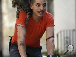 Bicyclist Rudi Saldia and his cat Mary Jane pose for a portrait during an interview with the Associated Press in Philadelphia. Saldia often buzzes around Philadelphia with his year-old feline Mary Jane perched on his shoulder. Their urban adventures have turned heads on the street and garnered big hits on YouTube. (AP Photo/Matt Rourke)