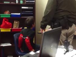 In this image made from video taken in August 2014, and provided by the American Civil Liberties Union on Tuesday, Aug. 4, 2015, an 8-year-old boy struggles and cries out as he sits in a chair with handcuffs around his biceps and his arms locked behind him while a school resource officer stands nearby, at an elementary school in Covington, Ky. (American Civil Liberties Union via AP)