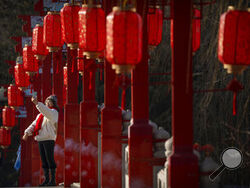 A woman poses for a selfie on a bridge decorated with lanterns at a public park in Beijing on the first day of the Lunar New Year holiday, Sunday, Jan. 22, 2023. (AP Photo/Mark Schiefelbein)