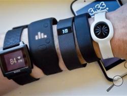 In this Dec. 15, 2014 file photo, fitness trackers, from left, Basis Peak, Adidas Fit Smart, Fitbit Charge, Sony SmartBand, and Jawbone Move, are posed for a photo next to an iPhone, in New York. (AP Photo/Bebeto Matthews, File)