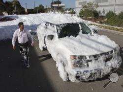 Marco Guerra checks out his car after driving it through chemical foam used as a fire retardant that spilled out from a hangar at San Jose International Airport in San Jose, Calif., Friday, Nov. 18, 2016. A bobbing sea of white foam several feet deep in spots spewed out of a large hangar at the airport, covering cars and blocking businesses as it cascaded onto a nearby street. (Patrick Tehan/Bay Area News Group via AP)