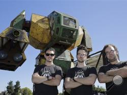 In this photo taken Friday, Oct. 9, 2015, MegaBots founders from left, Brinkley Warren, Matt Oehrlein and Gui Cavalcanti stand below their 15-foot tall, piloted Mk.II robot at the Pioneer Summit in Redwood City, Calif. (AP Photo/Eric Risberg)