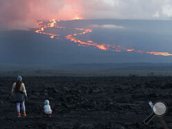 FILE - Spectators watch the lava flow down the mountain from the Mauna Loa eruption, Nov. 29, 2022, near Hilo, Hawaii. On Wednesday, Dec. 7, the lava from Mauna Loa, was 1.8 miles from Saddle Road, also known as Route 200 or Daniel K. Inouye Highway, scientists with the U.S. Geological Survey said. (AP Photo/Marco Garcia, File)