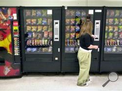 A student buys a brown sugar Pop-Tart from a vending machine in the hallway outside the school cafeteria in Wichita, Kan. High-calorie sports drinks and candy bars will be removed from school vending machines and cafeteria lines as soon as next year, replaced with diet drinks, granola bars and other healthier items the Agriculture Department said Thursday. (AP Photo/The Wichita Eagle, Mike Hutmacher, File)