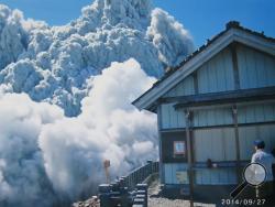 In this Saturday, Sept. 27, 2014 file photo taken by 59-year-old hiker Izumi Noguchi who fell victim to the eruption of Mount Ontake, and was offered to Kyodo News by his wife, Hiromi, Friday, Oct. 3, a hiker standing on the summit shrine compound on Mount Ontake watches dense plumes of gases and ash billowing from the crater as the volcanic mountain starts to erupt in central Japan. Construction company employee Noguchi was climbing alone, as his usual hiking companion, his wife Hiromi, had to work, she to