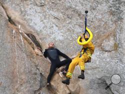 In this photo provided by Bob Isenberg, Michael Banks is stranded on a ledge some 80 feet off the ground on Morro Rock, a landmark in Morro Bay, Calif., Thursday, April 7, 2016. He had scaled the rock to make an Internet proposal to his girlfriend - who said yes - but then got stuck on a ledge and couldn't get down. A helicopter had to be called, and Morro Bay Fire Department Capt. Todd Gailey was lowered by cable to pluck Banks and take him to safety.(Bob Isenberg via AP)