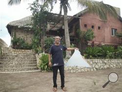 Tony Manna, a hotel owner in the Mozambican coastal town of Vilankulo, stands in front of his hotel, the Varanda, in late February, 2016 with what may be a piece of a missing Malaysian airliner that was discovered on a nearby sandbank. Manna says he connected Blaine Gibson, an American looking for debris, with a local boat operator who took him to the sandbank where the pair found the possible piece of the missing plane. Malaysia Airlines Flight 370 disappeared March 8, 2014. (Blaine Gibson via AP)