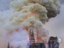 Flames and smoke rise as the spire on Notre Dame cathedral collapses in Paris, Monday, April 15, 2019. Massive plumes of yellow brown smoke is filling the air above Notre Dame Cathedral and ash is falling on tourists and others around the island that marks the center of Paris. (AP Photo/Diana Ayanna)