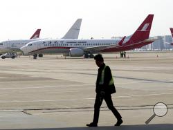 A ground crew walks near a Boeing 737 Max 8 plane operated by Shanghai Airlines parked on the tarmac at Hongqiao airport in Shanghai, China, Tuesday, March 12, 2019. U.S. aviation experts on Tuesday joined the investigation into the crash of an Ethiopian Airlines jetliner that killed 157 people, as a growing number of airlines grounded the new Boeing plane involved in the crash. (AP Photo)