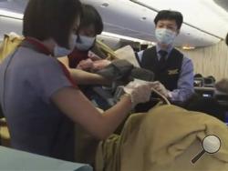 In an image from AP video, a member of the plane's crew holds up a newborn after Dr. Angelica Zen, who is obscured at lower right, delivered the baby on a China Air flight from Taiwan on Oct. 7, 2015. A passenger had gone into labor, and the flight was diverted to Alaska. Mother and newborn daughter left for a hospital, and the flight continued on to Los Angeles. (Edmund Chen/AP Video via AP Photo)