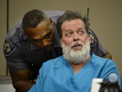 An El Paso County Sheriff's Deputy talks to Robert Lewis Dear during a court appearance on Wednesday, Dec. 9, 2015, in Colorado Springs, Colo. Dear, accused of killing three people and wounding nine others at a Colorado Springs Planned Parenthood clinic on Nov. 27, was charged with first-degree murder. (Andy Cross/The Denver Post via AP, Pool)