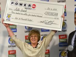 In this Oct. 6, 2015 file photo, Julie Leach of of Three Rivers, Mich., holds her $310 Million Powerball jackpot check, accompanied by Michigan Lottery Commissioner M. Scott Bowen in Lansing, Mich. (Dale G. Young/The Detroit News via AP, File)