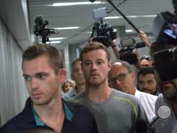 Accompanied by Brazilian lawyer Sergio Viegas, second from right, American Olympic swimmers Gunnar Bentz, center, and Jack Conger, right, leave the police station at Rio International airport early Thursday Aug. 18, 2016. The two were taken off their flight from Brazil to the U.S. on Wednesday by local authorities amid an investigation into a reported robbery targeting Ryan Lochte and his teammates. (AP Photo/Mauro Pimentel)