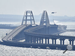 A helicopter drops water to stop fire on Crimean Bridge connecting Russian mainland and Crimean peninsula over the Kerch Strait, in Kerch, Saturday, Oct. 8, 2022. Russian authorities say a truck bomb has caused a fire and the collapse of a section of a bridge linking Russia-annexed Crimea with Russia. The bridge is a key supply artery for Moscow's faltering war effort in southern Ukraine. (AP Photo)