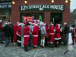 Santacon participants lineup outside a lower eastside bar on Saturday, Dec. 14, 2013 in New York. Thousands of red-suited revelers spread out through the city's bars and snowy streets amid criticism that the event has become too rowdy. (AP Photo/Bebeto Matthews)
