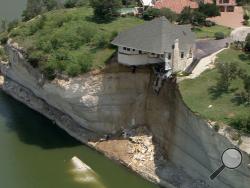 In this image taken from video provided June 12, 2014, by WFAA.Com, a luxury house teeters on a cliff about 75 feet above Lake Whitney in Whitney, Texas. The owner of a vacant luxury house teetering on a crumbling 75-foot cliff over a Central Texas lake has decided to burn the house and clear the lot of the debris. (AP Photo/WFAA.Com) 