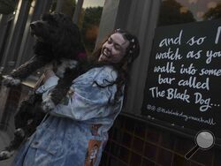 Taylor Swift fan Brodie MacArthur from east London poses with a friend's dog next to a sign featuring Taylor Swift lyrics outside The Black Dog pub in Vauxhall, London, Saturday, May 4, 2024. As Taylor Swift prepares to launch the Europe leg of her blockbuster Eras tour, thousands of her fans from the U.S. and Canada are following her across the pond. (AP Photo/Alastair Grant)