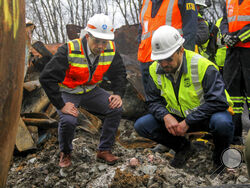 Transportation Secretary Pete Buttigieg, left, and Tristan Brown, deputy administrator of the Pipeline and Hazardous Materials Safety Administration, crouch down to look at part of a burned traincar, Thursday, Feb. 23, 2023, in East Palestine, Ohio, at the site of a Norfolk Southern train derailment. (Allie Vugrincic/The Vindicator via AP, Pool)