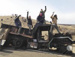 In this Monday, Nov. 21, 2016, file photo, protesters against the Dakota Access oil pipeline stand on a burned-out truck near Cannon Ball, N.D., that they removed from a long-closed bridge a day earlier on a state highway near their camp in southern North Dakota. President-elect Donald Trump holds stock in the company building the disputed Dakota Access oil pipeline, and pipeline opponents warn that Trump’s investments could undercut any decision he makes on the $3.8 billion project as president. (AP Photo/