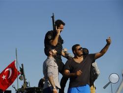 A Turkish man takes a selfie with a Turkish police officer, loyal to the government, as they stand atop tanks abandoned by Turkish army officers, against a backdrop of Istanbul's iconic Bosporus Bridge, Saturday, July 16, 2016. Turkish President Recep Tayyip Erdogan told the nation Saturday that his government is in charge after a coup attempt brought a night of explosions, air battles and gunfire across the capital that left dozens dead. (AP Photo/Emrah Gurel)