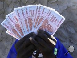 A man holds a handful of 5 Billion Zimbabwean dollar notes, in Harare, Friday, June, 12, 2015. Zimbabwe's central bank says banknotes from its old currency, which collapsed and was discarded years ago because of runaway inflation, can be exchanged for American dollars. But 100 trillion Zimbabwean dollars will fetch only 40 U.S. cents. (AP Photo/Tsvangirayi Mukwazhi)