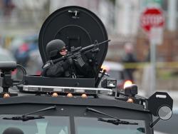 Police in tactical gear arrive on an armored police vehicle as they surround an apartment building while looking for a suspect in the Boston Marathon bombings in Watertown, Mass., Friday, April 19, 2013. The bombs that blew up seconds apart near the finish line of the Boston Marathon left the streets spattered with blood and glass, and gaping questions of who chose to attack and why. (AP Photo/Charles Krupa) 