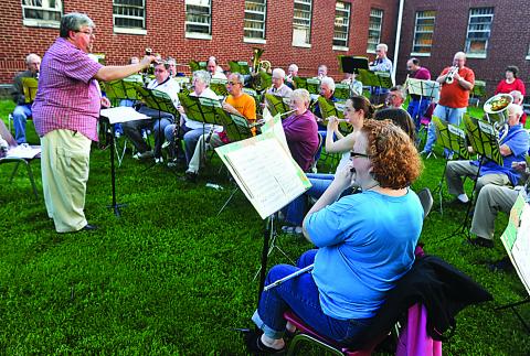 Under the direction of John Collins, left, the Danville Community Band rehearses for their upcoming concert on the lawn of the Kirkbride building on the Danville State Hospital grounds Thursday evening. The band will perform their annual spring concert on Thursday, May 16 at 7 p.m. at Trinity Lutheran Church in Danville.