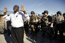 A community activist tries to persuade a group of protesters to move back as police in riot gear watch protesters in Ferguson, Mo. on Wednesday, Aug. 13, 2014. On Saturday, Aug. 9, 2014, a white police officer fatally shot Michael Brown, an unarmed black teenager, in the St. Louis suburb. (AP Photo/Jeff Roberson)