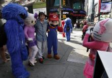 A man has his photo taken by a Hello Kitty character, right, as he poses with Cookie Monster, another Hello Kitty and Super Mario characters, in New York's Times Square, Tuesday, April 9, 2013. A string of arrests in the last few months has brought unwelcome attention to the growing number of people, mostly poor immigrants, who make a living by donning character outfits, roaming Times Square and charging tourists a few dollars to pose with them in photos. (AP Photo/Richard Drew)