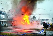 Firefighters set up hoses as the home of Gwen Zubler at 304 East Eighth St. in Bloomsburg collapses in a ball of fire on Tuesday morning. The fire is spreading to the next door home of Larry Poust, at left, at 312 East Eighth Street. 