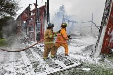 Firefighters walk across a front wall that has come down as they enter a studio area in the front of a large pole barn during Wednesday morning’s fire at 148 Karns Road in Benton Township. (Press Enterprise/Jimmy May)